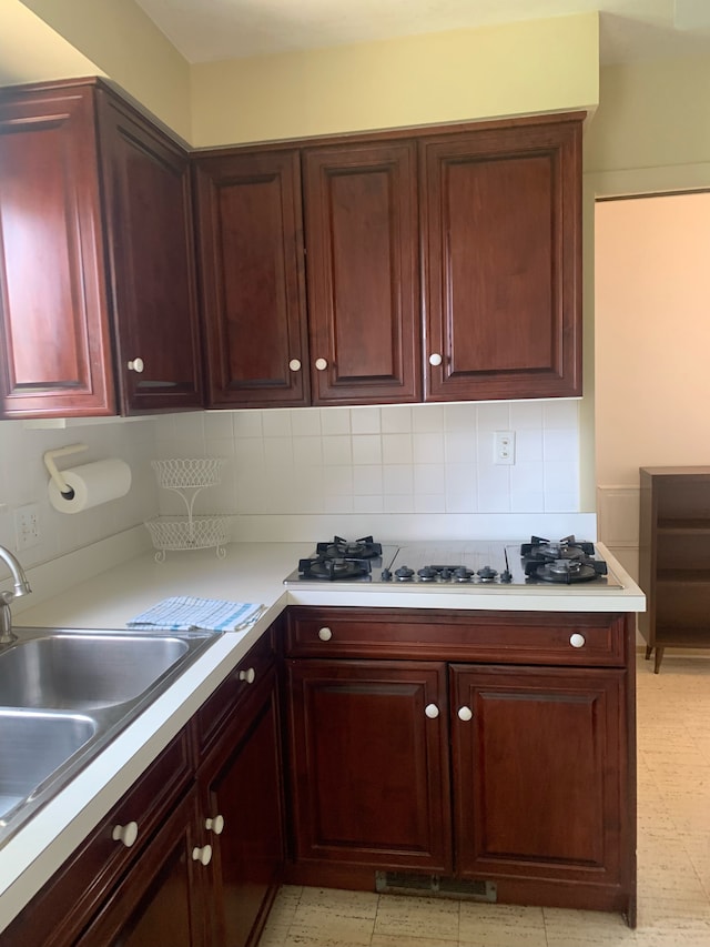 kitchen with light countertops, cooktop, decorative backsplash, and a sink
