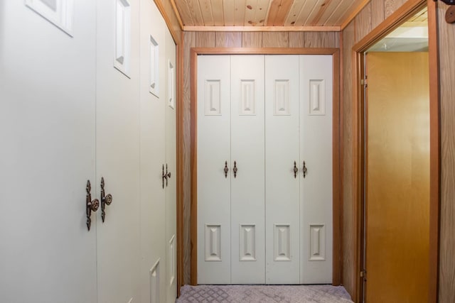 corridor with wood walls, wood ceiling, and light carpet