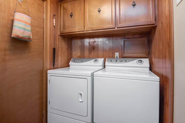 washroom featuring separate washer and dryer, wood walls, and cabinet space