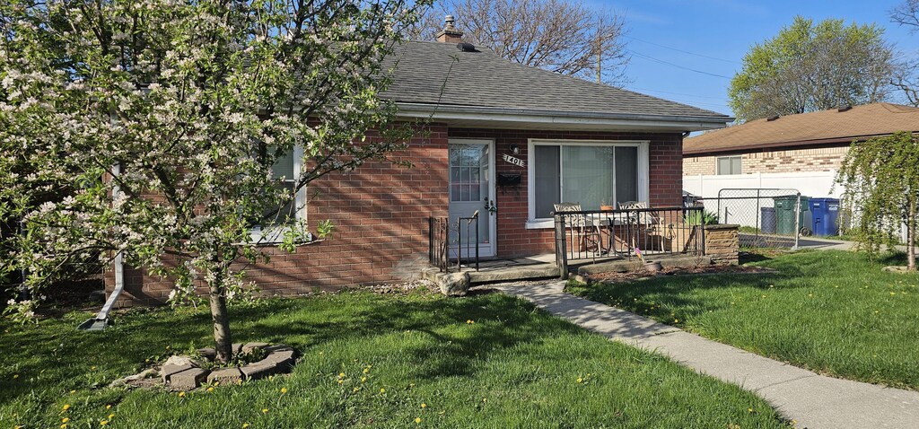 view of front of property featuring a front yard, roof with shingles, fence, and brick siding