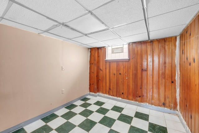 below grade area with wooden walls, tile patterned floors, and baseboards