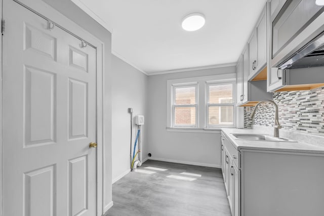 kitchen with light wood finished floors, a sink, tasteful backsplash, crown molding, and light countertops