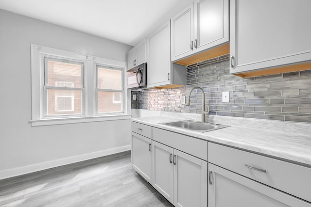 kitchen featuring stainless steel microwave, a sink, light countertops, baseboards, and backsplash