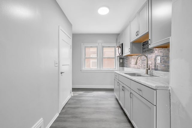 kitchen featuring stainless steel microwave, a sink, tasteful backsplash, baseboards, and light countertops