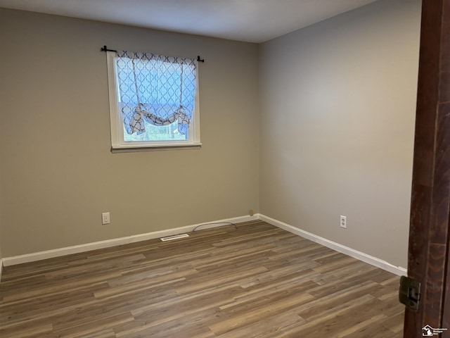 unfurnished room featuring baseboards, visible vents, and wood finished floors