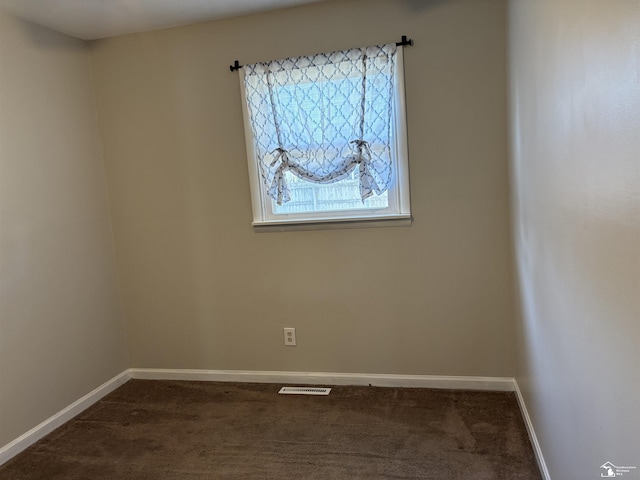 spare room featuring dark colored carpet, visible vents, and baseboards