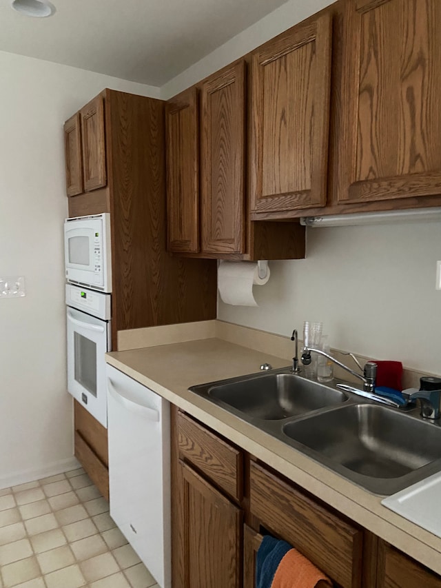 kitchen with white appliances, light countertops, brown cabinetry, and a sink