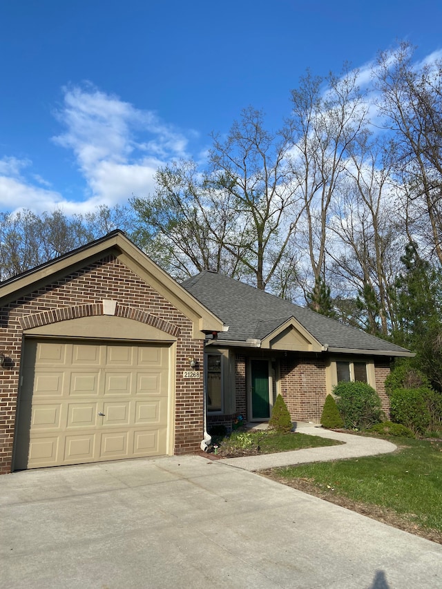 ranch-style home with a garage, brick siding, a shingled roof, and driveway