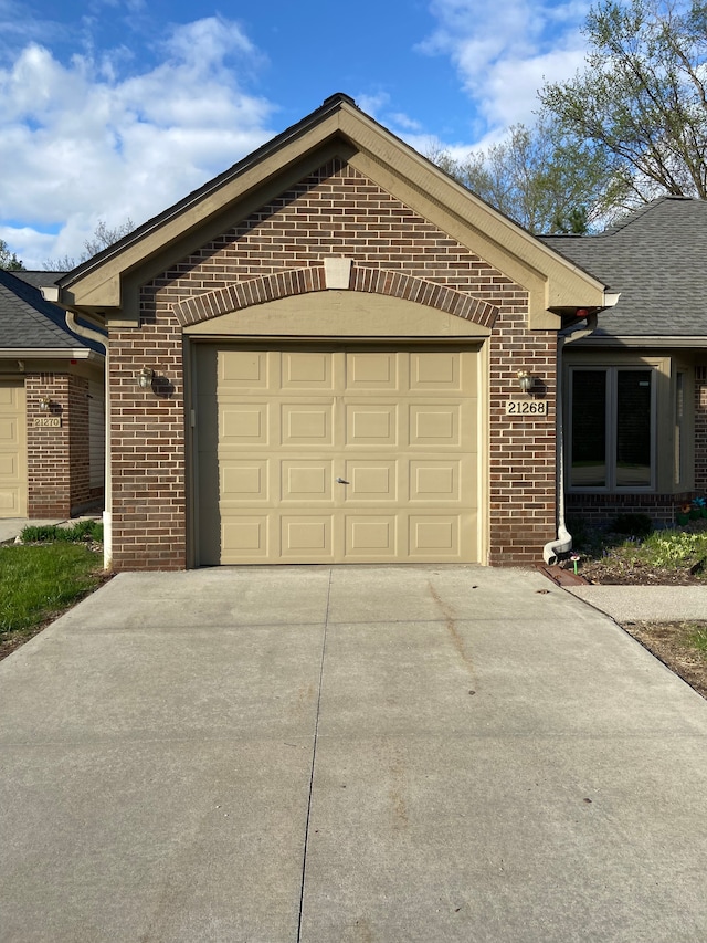 exterior space with concrete driveway, roof with shingles, an attached garage, and brick siding
