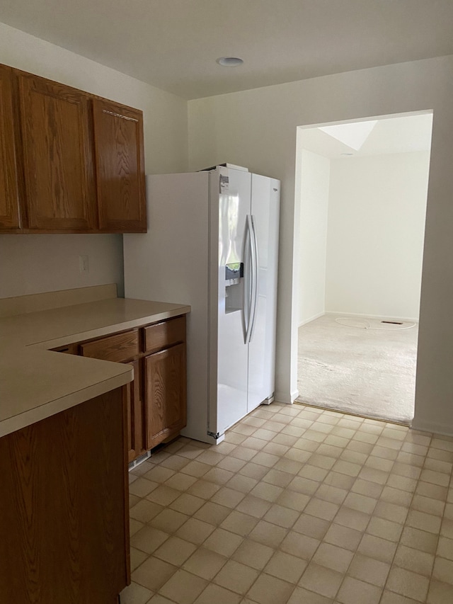 kitchen with white fridge with ice dispenser, brown cabinets, light colored carpet, and light countertops