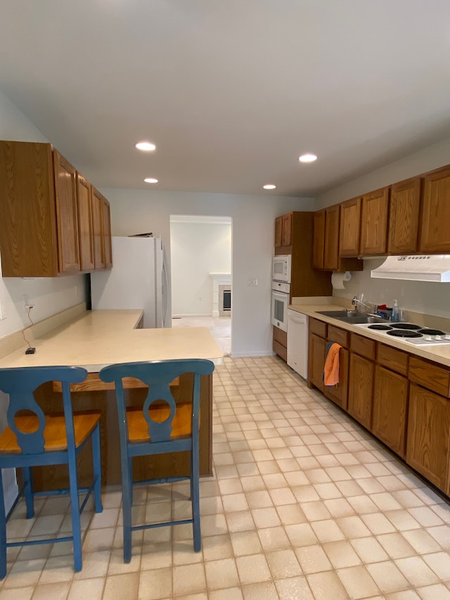 kitchen with brown cabinets, white appliances, light countertops, and under cabinet range hood