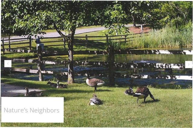 view of home's community featuring fence, a water view, and a yard