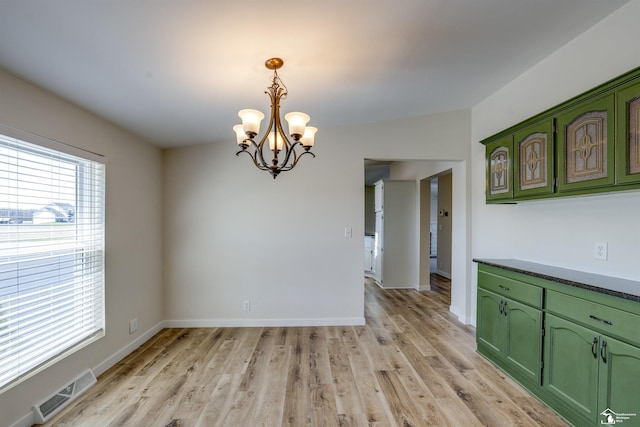 unfurnished dining area featuring light wood finished floors, an inviting chandelier, visible vents, and baseboards