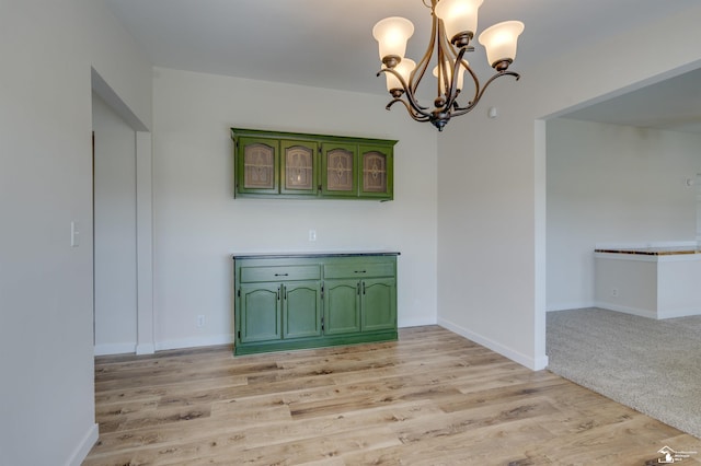 unfurnished dining area featuring light wood-style flooring, a notable chandelier, and baseboards