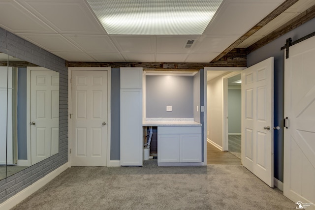 basement with a barn door, baseboards, visible vents, and light carpet