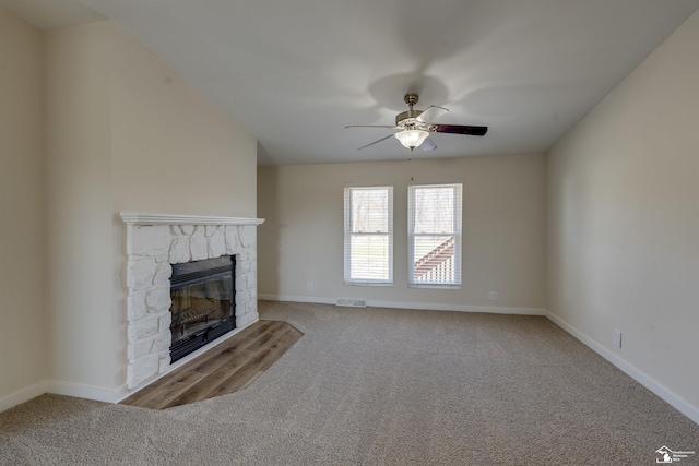unfurnished living room with baseboards, ceiling fan, a stone fireplace, and carpet flooring