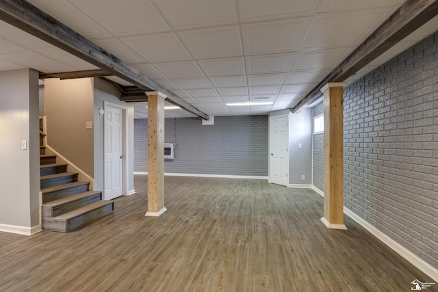 basement featuring baseboards, stairway, wood finished floors, and brick wall
