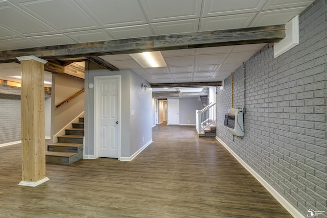 corridor with heating unit, wood finished floors, brick wall, baseboards, and stairway