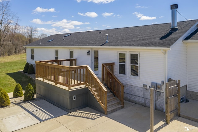 rear view of property featuring a wooden deck, a shingled roof, and a patio area