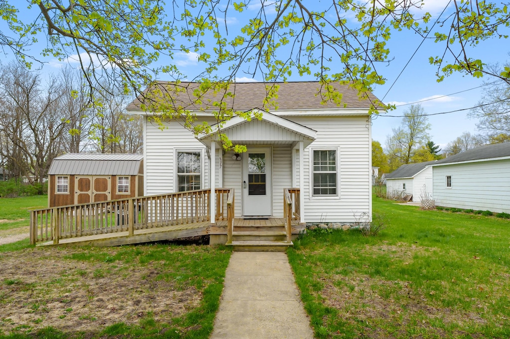 view of front of house with an outbuilding, a shed, a front lawn, and roof with shingles
