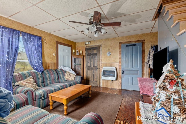 living area with heating unit, a paneled ceiling, and a ceiling fan