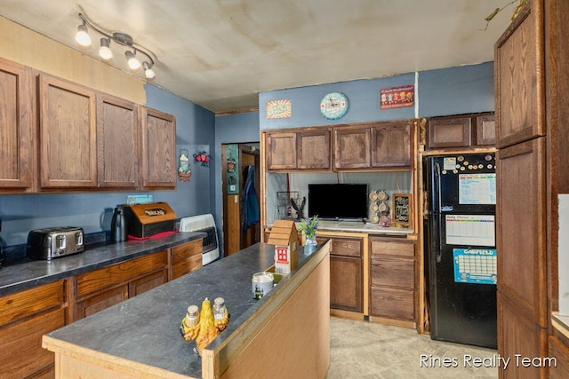 kitchen with freestanding refrigerator, dark countertops, and brown cabinetry