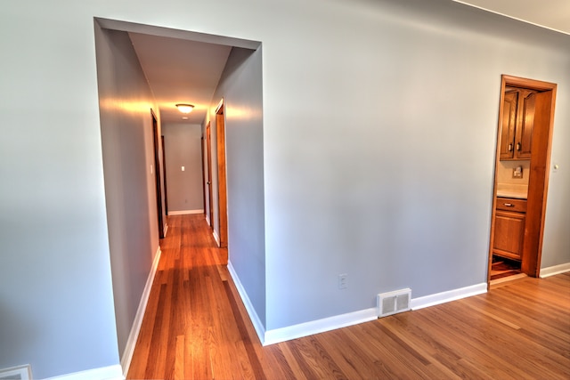 hall featuring baseboards, wood finished floors, and visible vents