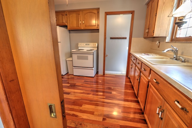 kitchen with brown cabinetry, wood finished floors, a sink, light countertops, and white appliances
