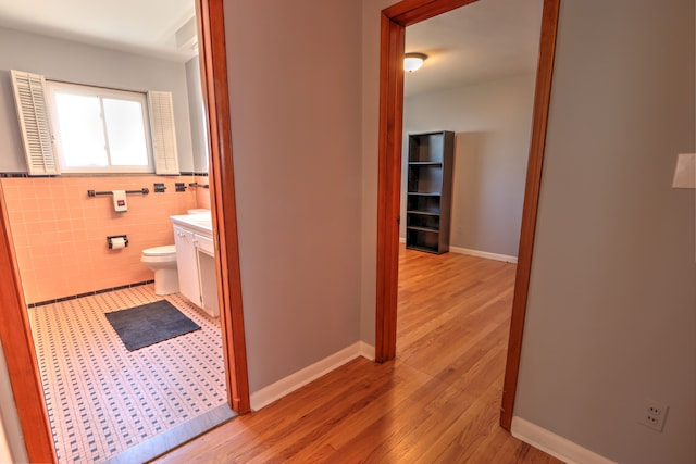 hall featuring light wood-style floors, baseboards, and tile walls