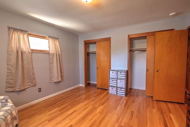 unfurnished bedroom with baseboards, multiple closets, and light wood-style flooring