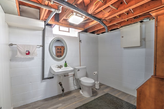 bathroom with toilet, concrete block wall, and wood finished floors