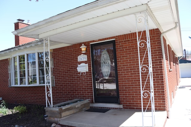 view of exterior entry featuring brick siding and a chimney