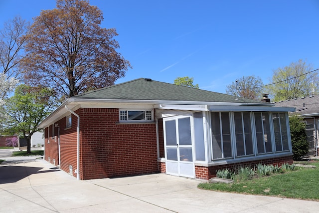 view of side of home with a shingled roof, a sunroom, and brick siding