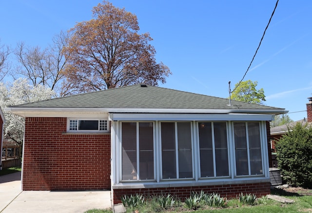 exterior space featuring brick siding, roof with shingles, a sunroom, and cooling unit