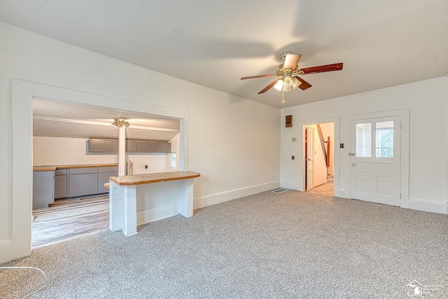 unfurnished living room featuring light colored carpet, visible vents, a ceiling fan, and baseboards