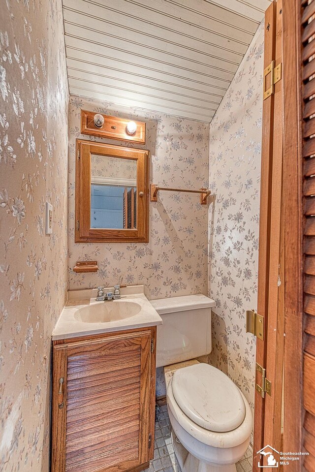 half bathroom with wallpapered walls, toilet, vanity, and wood ceiling