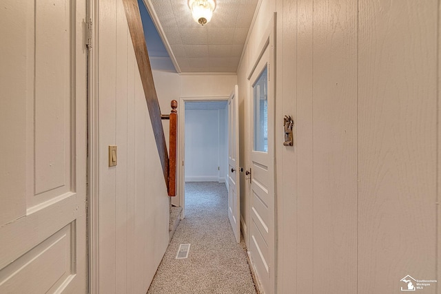 hall with visible vents, wooden walls, and light colored carpet