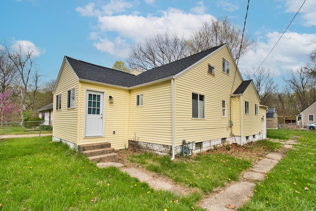 view of property exterior featuring fence, roof with shingles, a chimney, entry steps, and a lawn