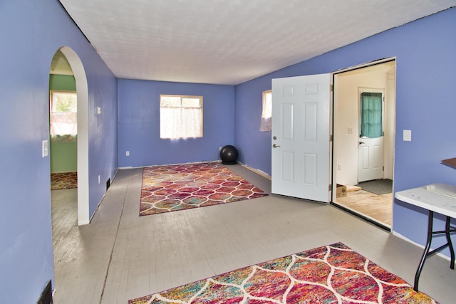 foyer entrance with baseboards, arched walkways, a textured ceiling, and a wealth of natural light
