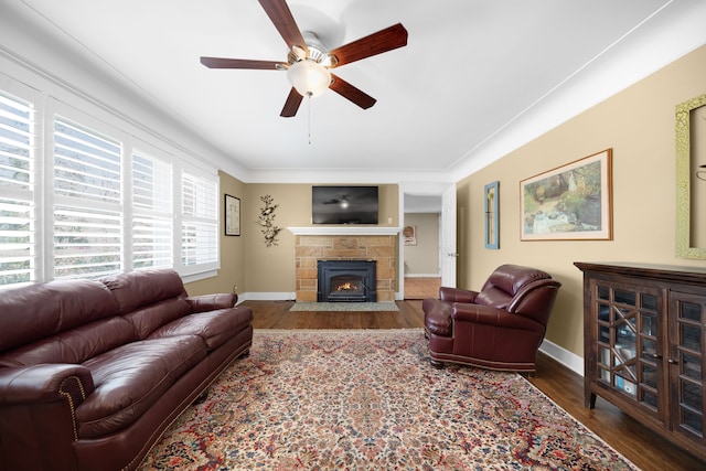 living area featuring a stone fireplace, a ceiling fan, baseboards, and wood finished floors