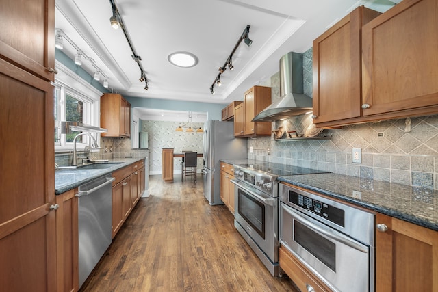kitchen with brown cabinets, appliances with stainless steel finishes, a sink, and wall chimney exhaust hood