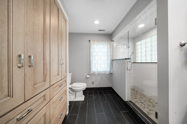 bathroom with a shower stall, toilet, wood finished floors, and visible vents