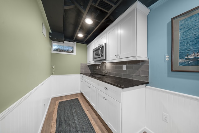 kitchen with dark wood-style flooring, wainscoting, stainless steel microwave, white cabinets, and a sink