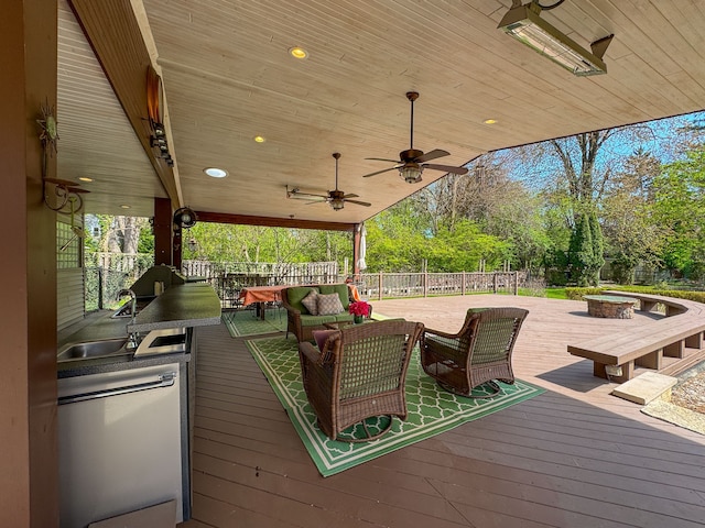 wooden deck featuring a sink, fence, a ceiling fan, and an outdoor living space with a fire pit