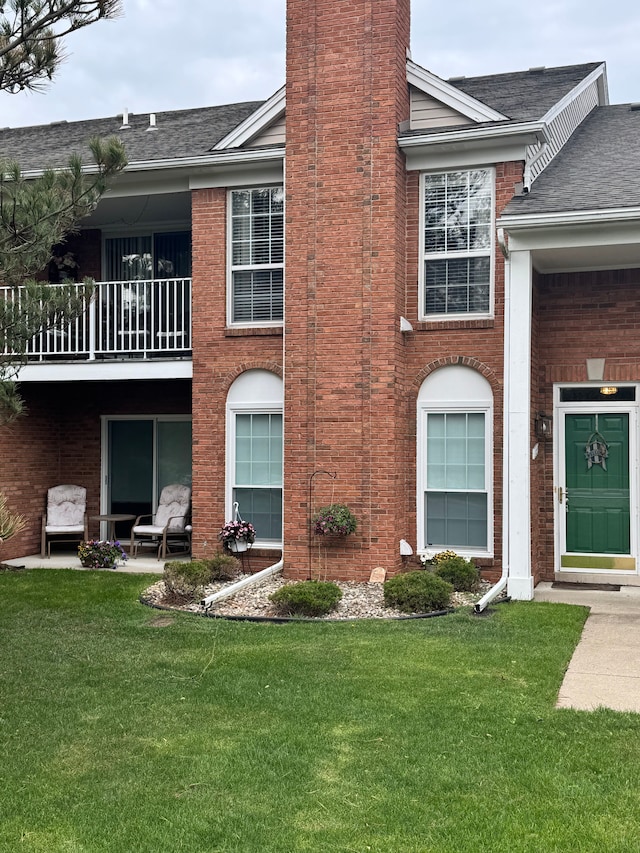 exterior space featuring a chimney, roof with shingles, a balcony, and a front yard