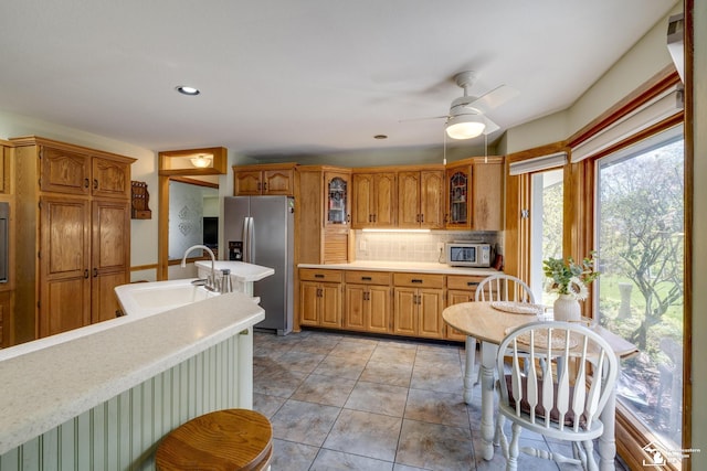 kitchen with decorative backsplash, glass insert cabinets, a sink, stainless steel appliances, and light countertops