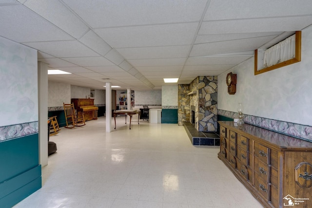 finished basement with a fireplace with raised hearth, a drop ceiling, and light floors