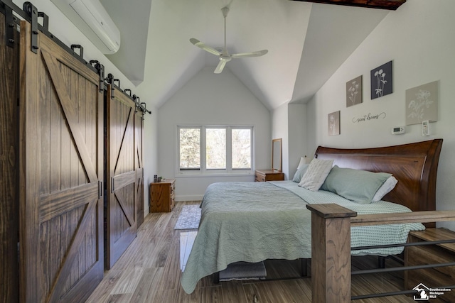 bedroom featuring a barn door, baseboards, a wall mounted AC, light wood finished floors, and vaulted ceiling