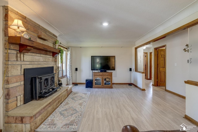 living room with light wood-type flooring, a wood stove, a textured ceiling, and baseboards