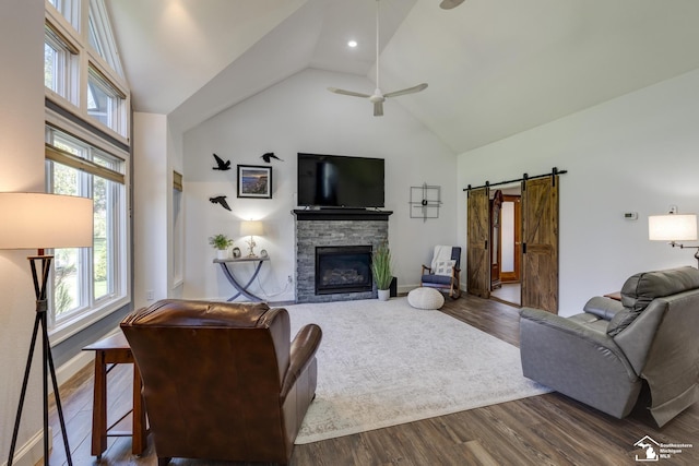 living room featuring a barn door, ceiling fan, a fireplace, wood finished floors, and high vaulted ceiling